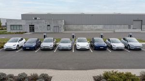 A row of modern electric vehicles parked on a clean lot with charging stations behind them representing the wave of EV lease returns in 2026